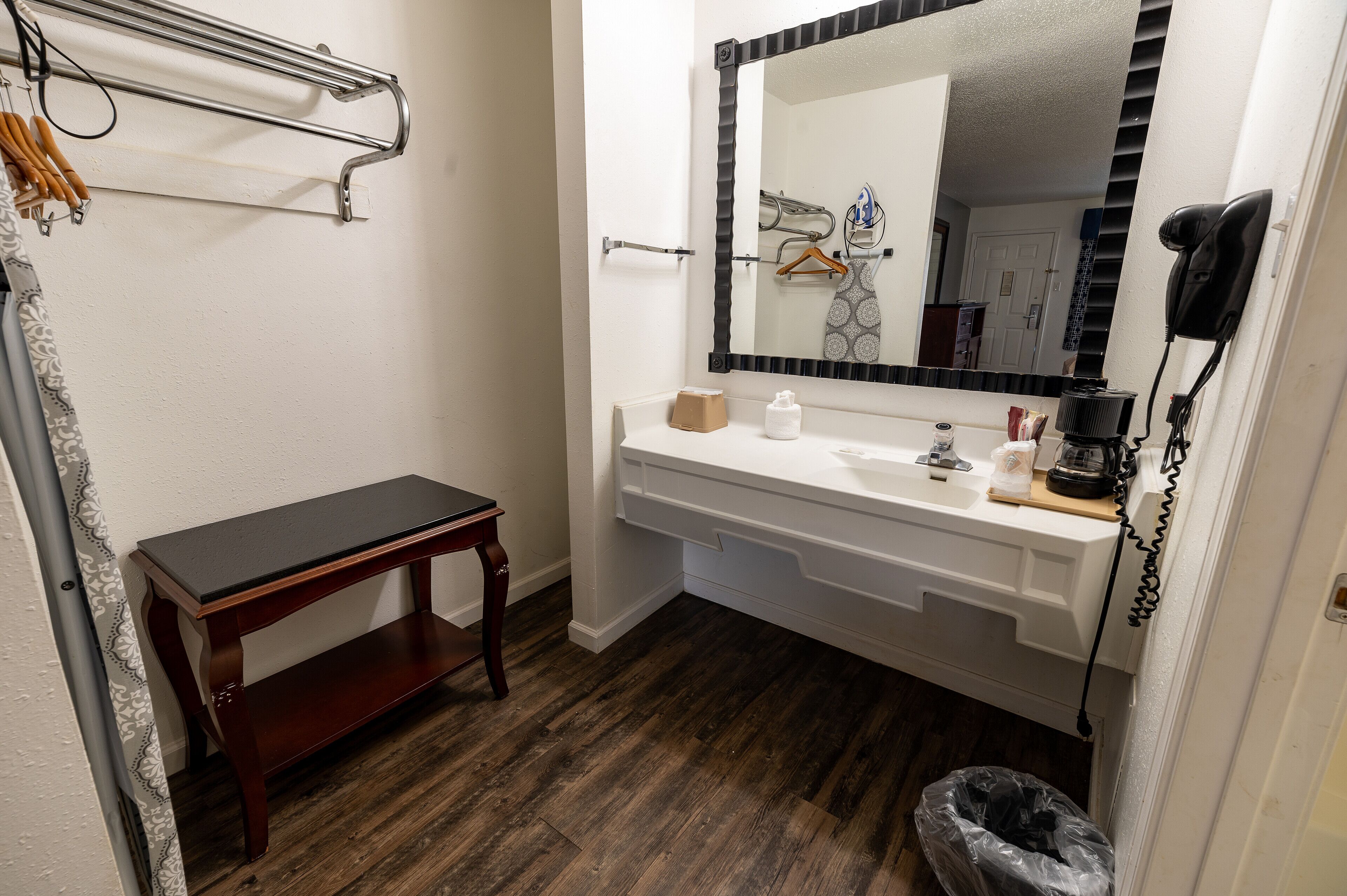 A bathroom with a wooden bench, a white sink, a mirror, and a hairdryer on the wall.