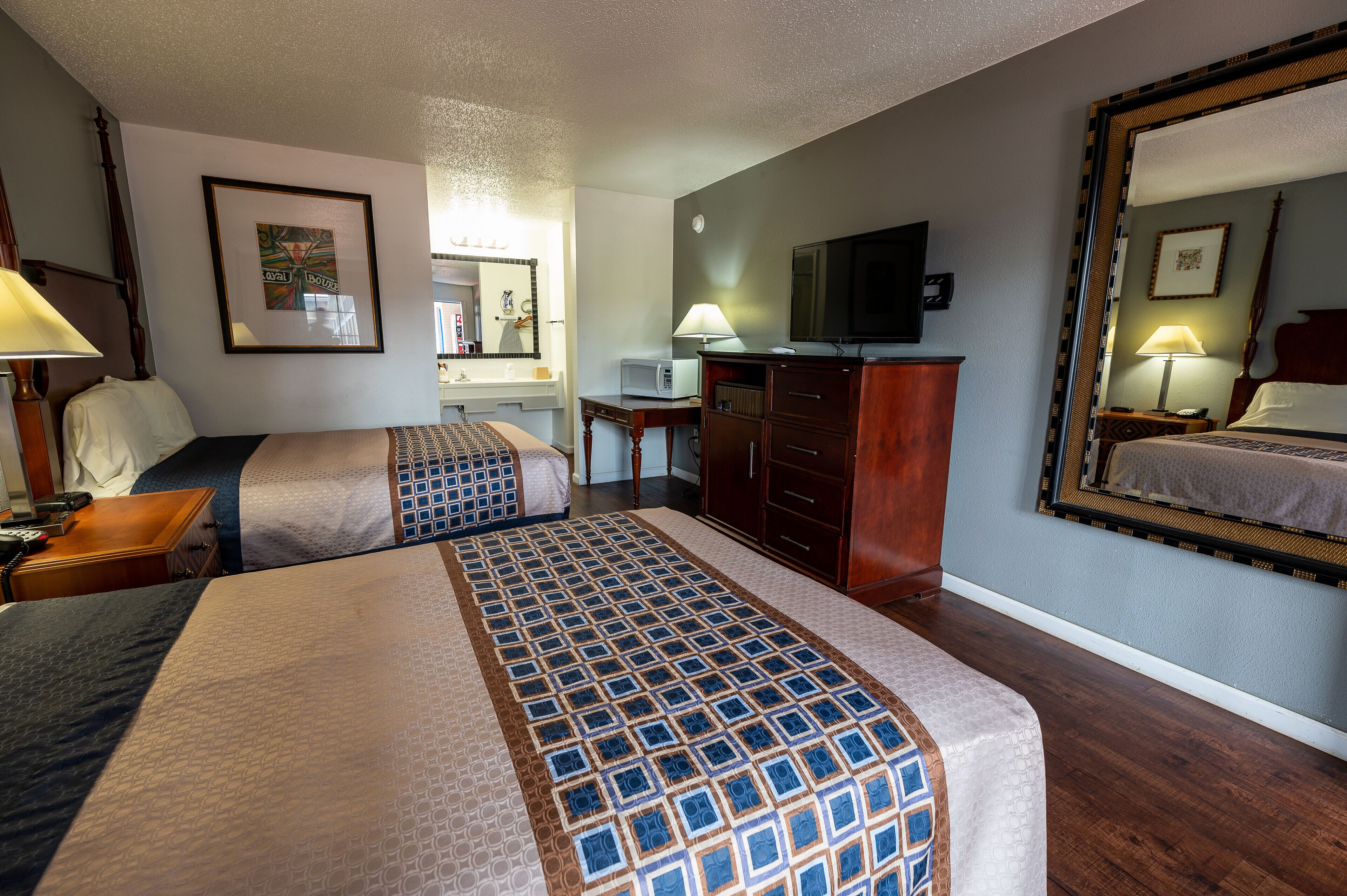 Una habitación de hotel con dos camas, un escritorio, un televisor y un espejo.