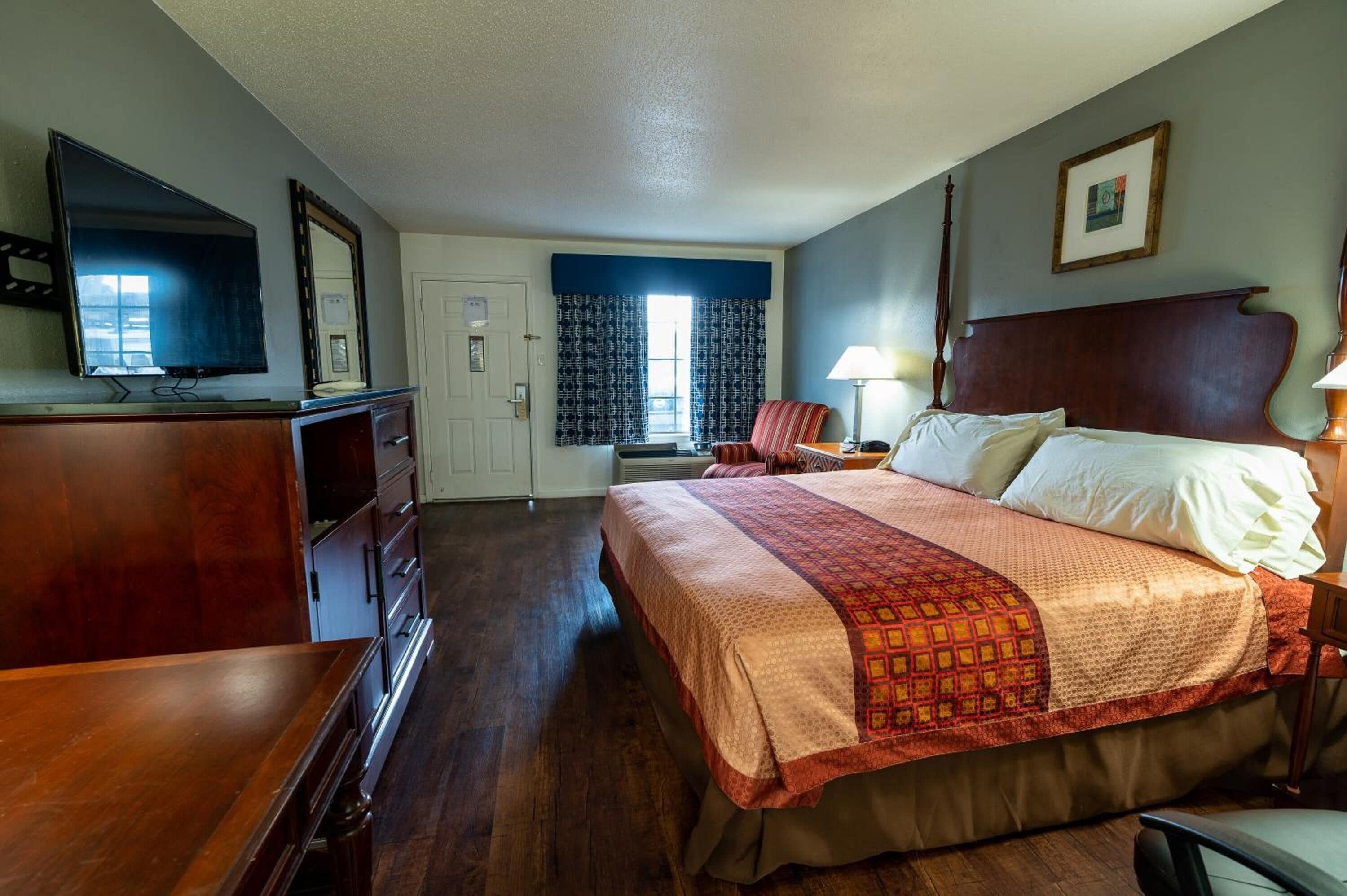 Habitación de hotel con cama, escritorio, silla, televisor y ventana con cortinas.