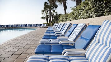Eine Reihe von gestreiften Liegestühlen am Pool, im Hintergrund Palmen.