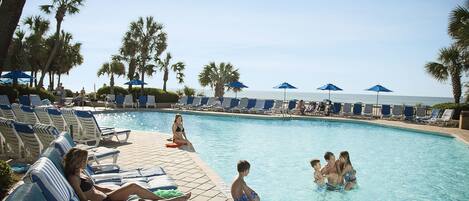 A poolside area with lounge chairs and umbrellas, a clear sky, and a calm pool.