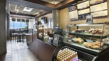 Una cafetería con una pizarra de menú, un escaparate con pasteles y una zona de estar con vistas.