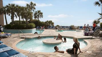 A pool area with multiple pools, lounge chairs, and palm trees.