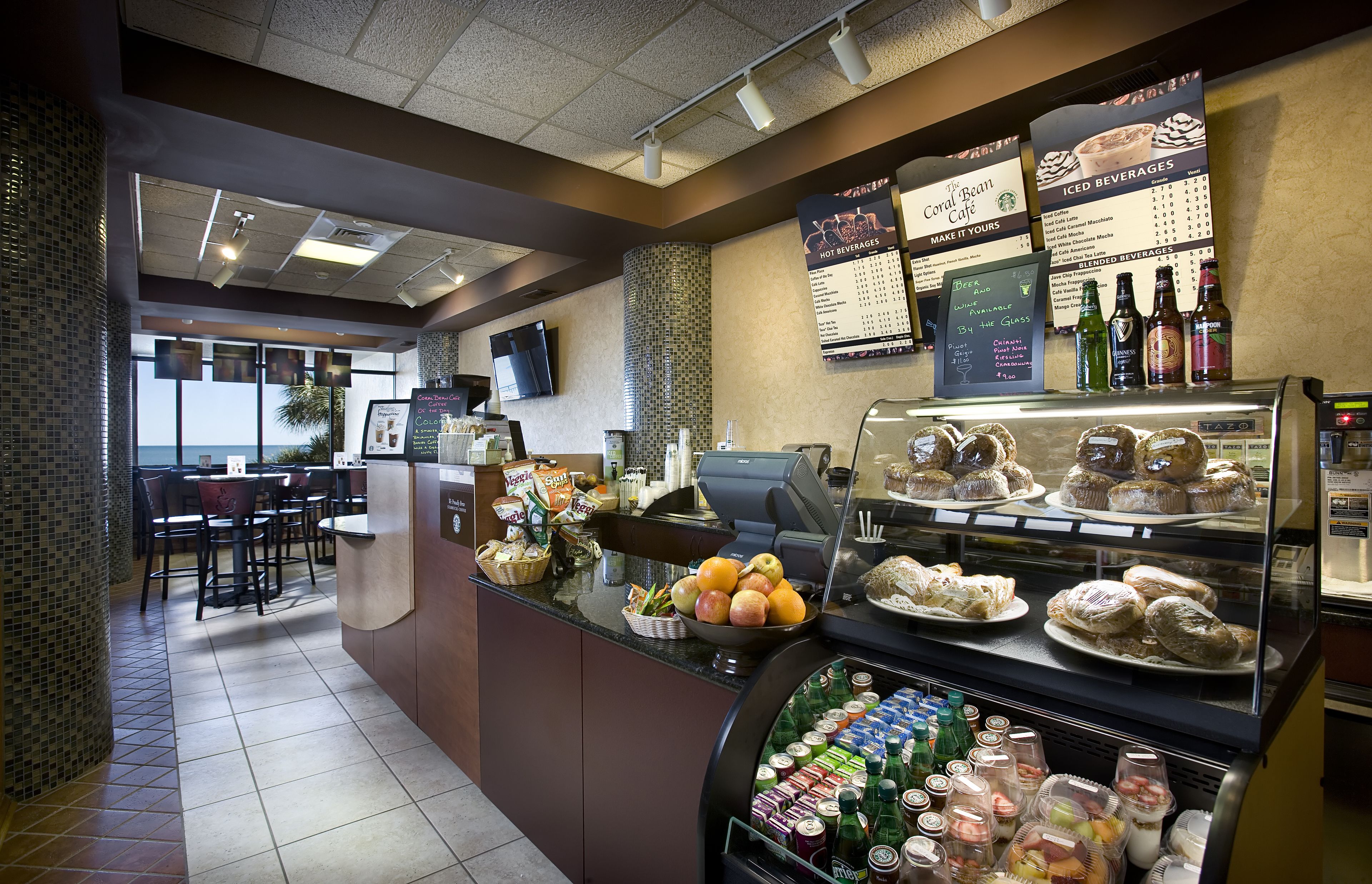 A cafe with a counter displaying pastries, a menu board, and a refrigerated display of beverages.