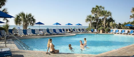 A pool area with lounge chairs and umbrellas, a clear sky, and palm trees.