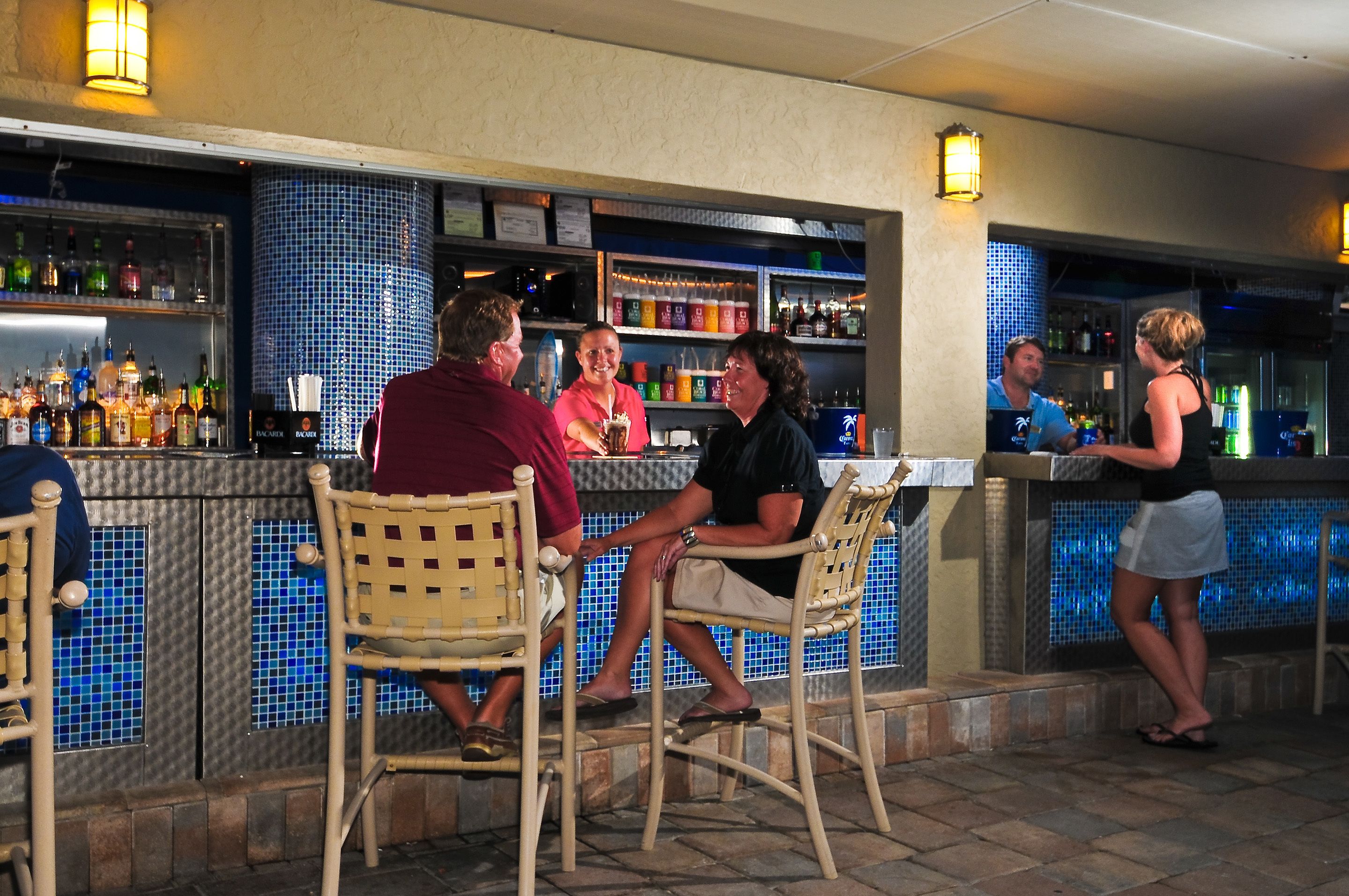 A bar area with wicker chairs, a tiled backsplash, and a variety of bottles on shelves.