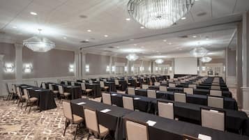 A large conference room with rows of tables and chairs, chandeliers, and a carpeted floor.