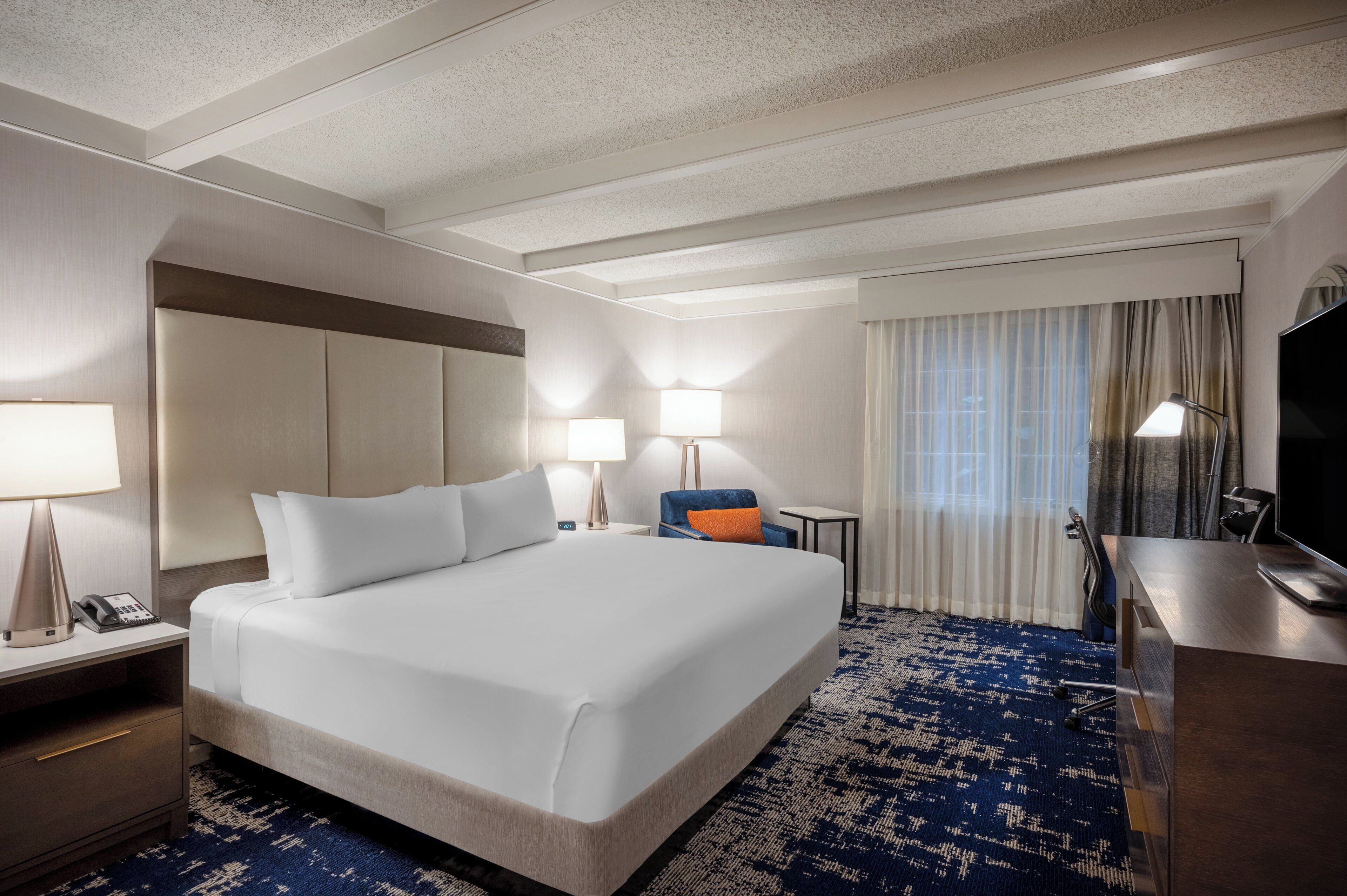 Habitación de hotel con una cama grande, dos lámparas de noche, un escritorio con televisión de pantalla plana y una alfombra azul estampada.
