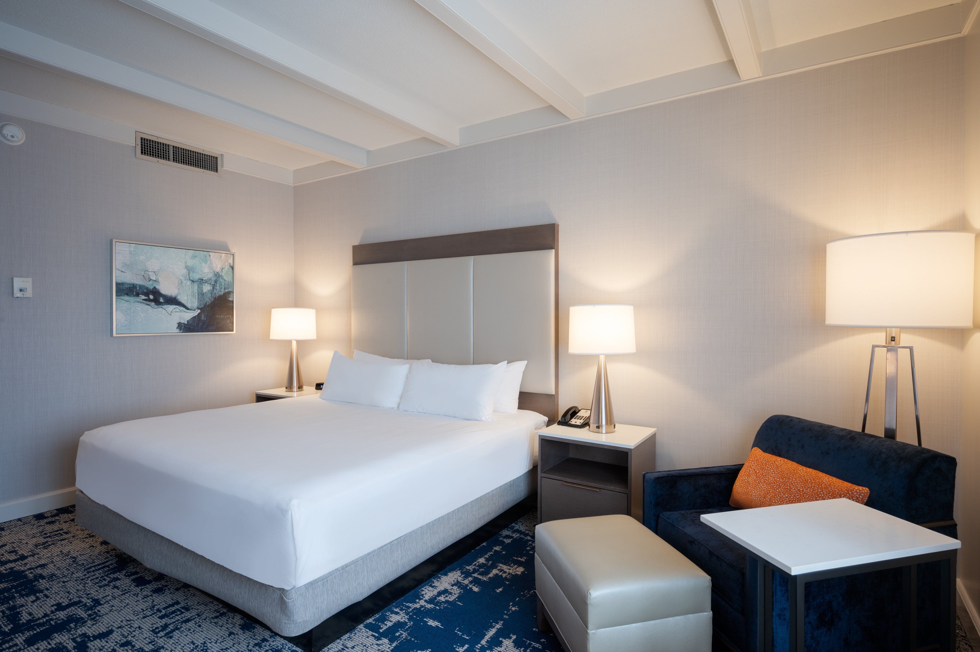 Une chambre d’hôtel avec un grand lit, deux tables de chevet avec des lampes, une chaise et une petite table.