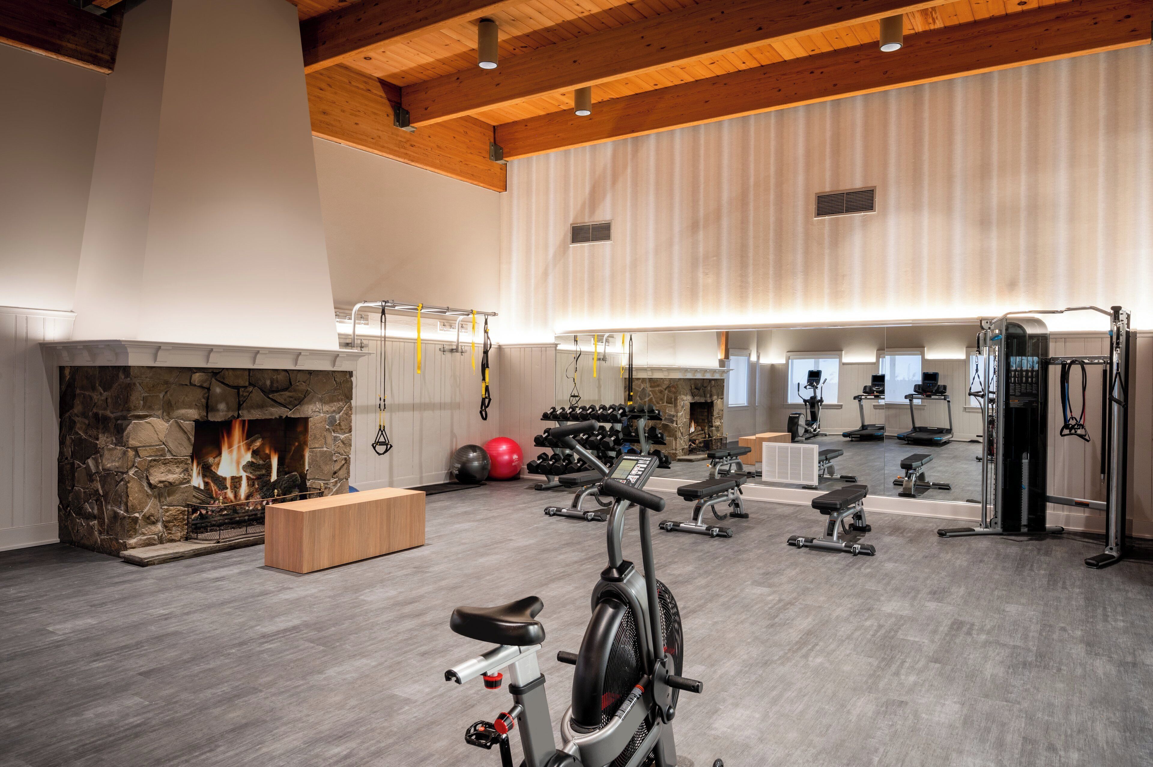 Un gimnasio amplio con chimenea de piedra, equipo de ejercicio y un espejo grande.