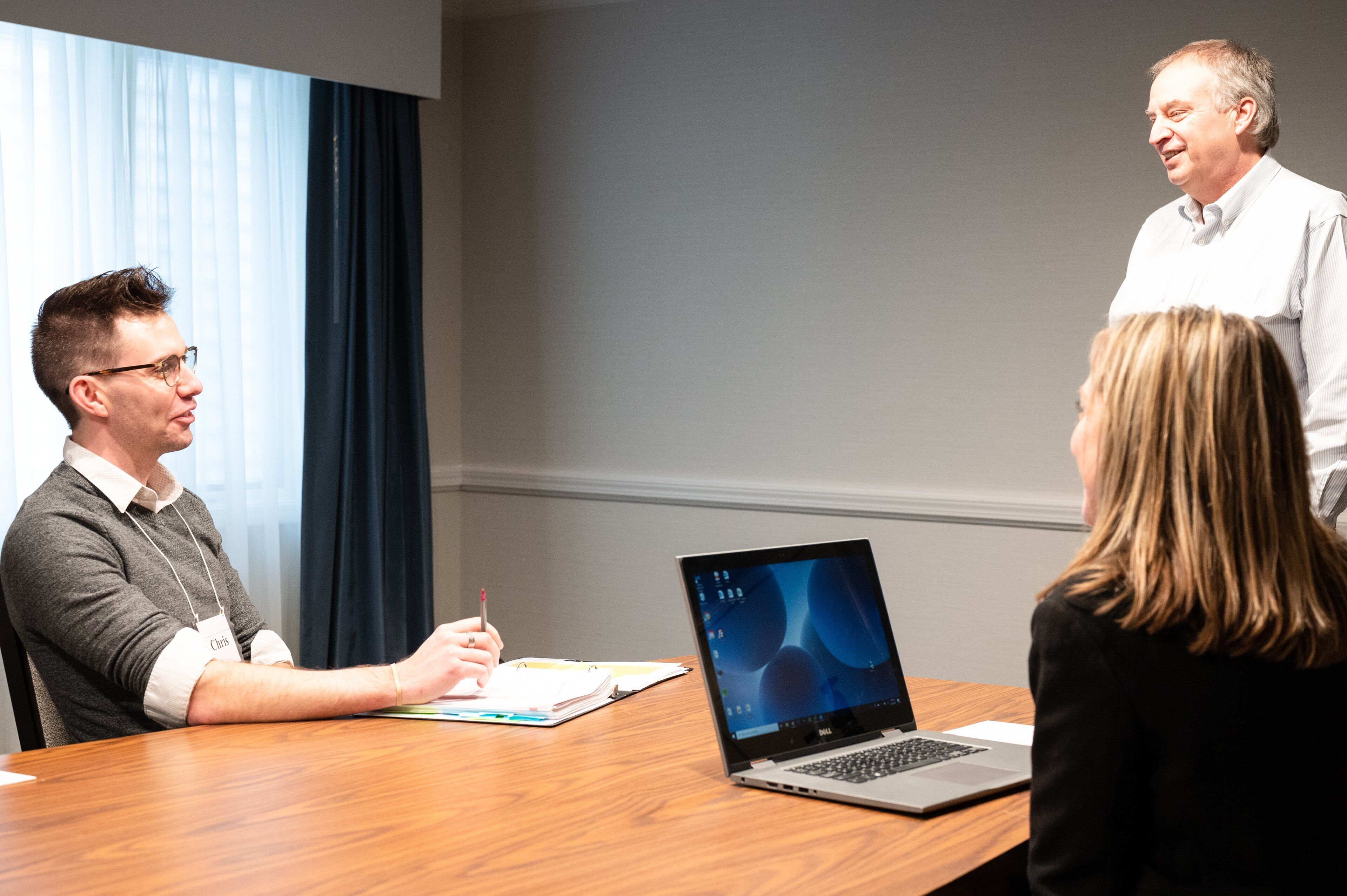 A conference room with a wooden table, a laptop, and a person writing.