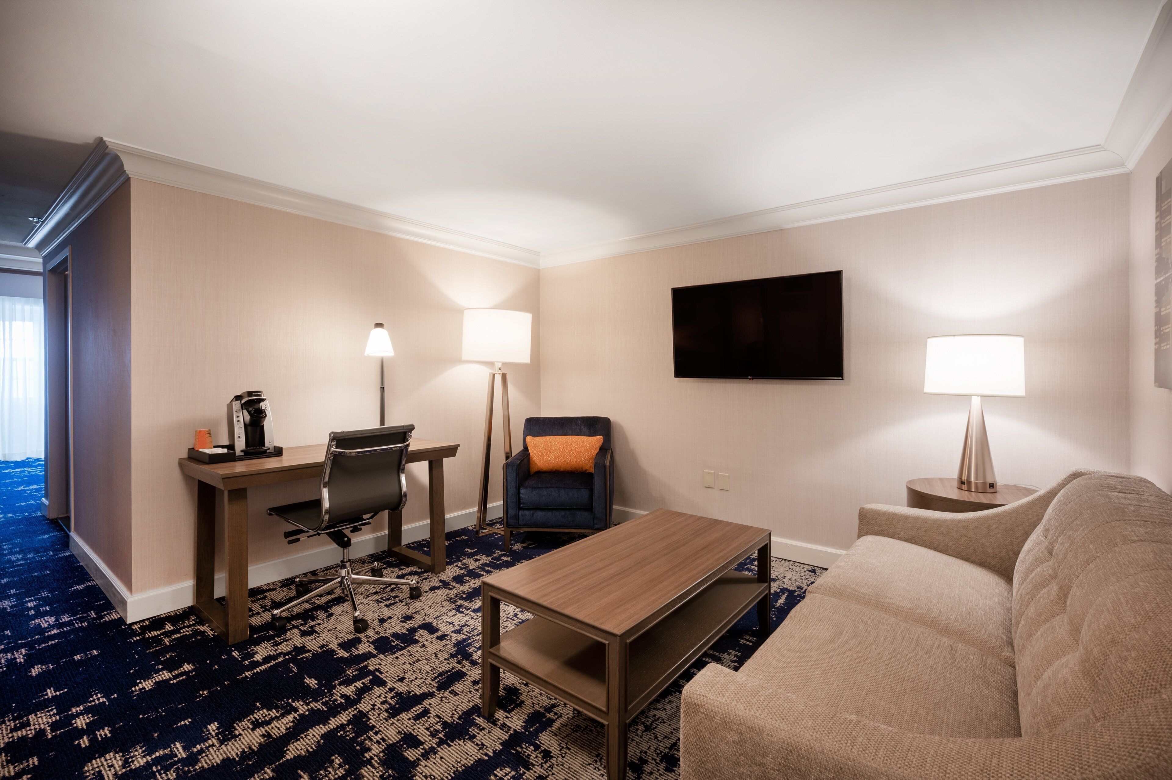 A hotel room with a desk, chair, sofa, and two lamps.