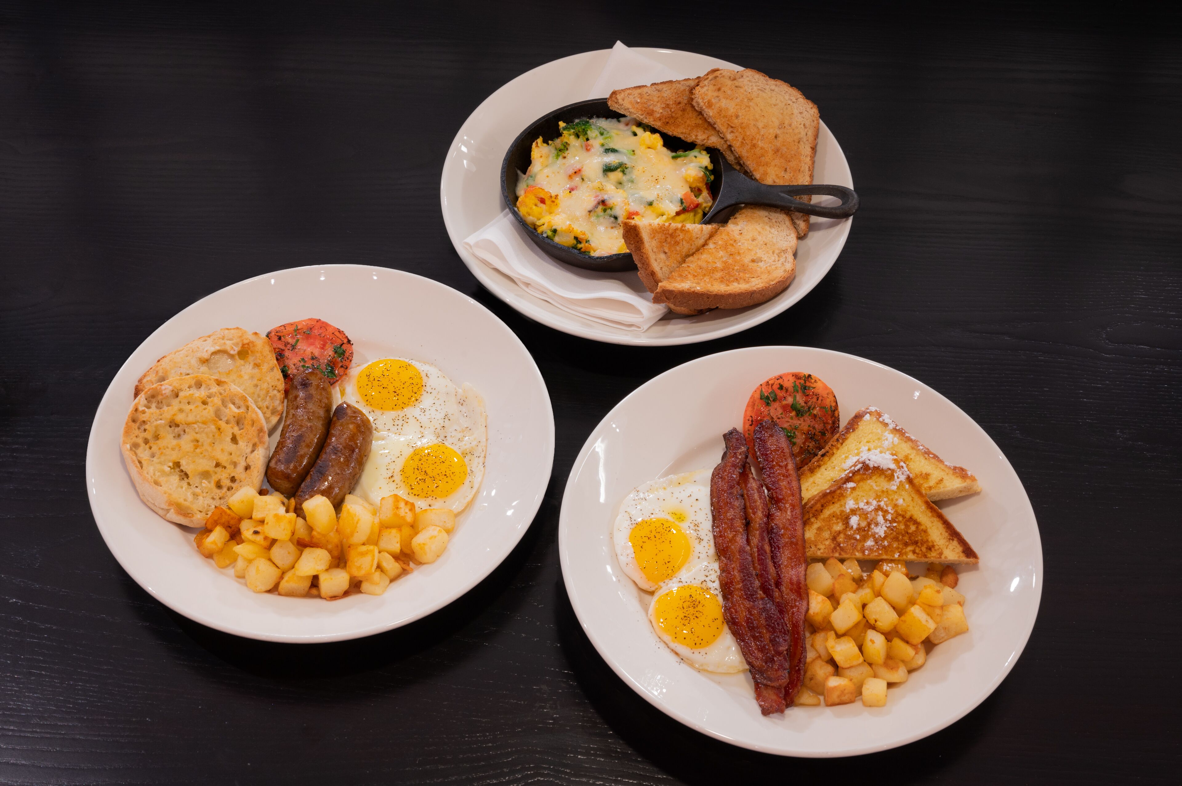 Three plates of breakfast food including eggs, sausages, toast, and potatoes.