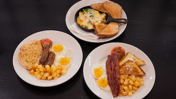 Three plates of breakfast food including eggs, sausages, toast, and potatoes.