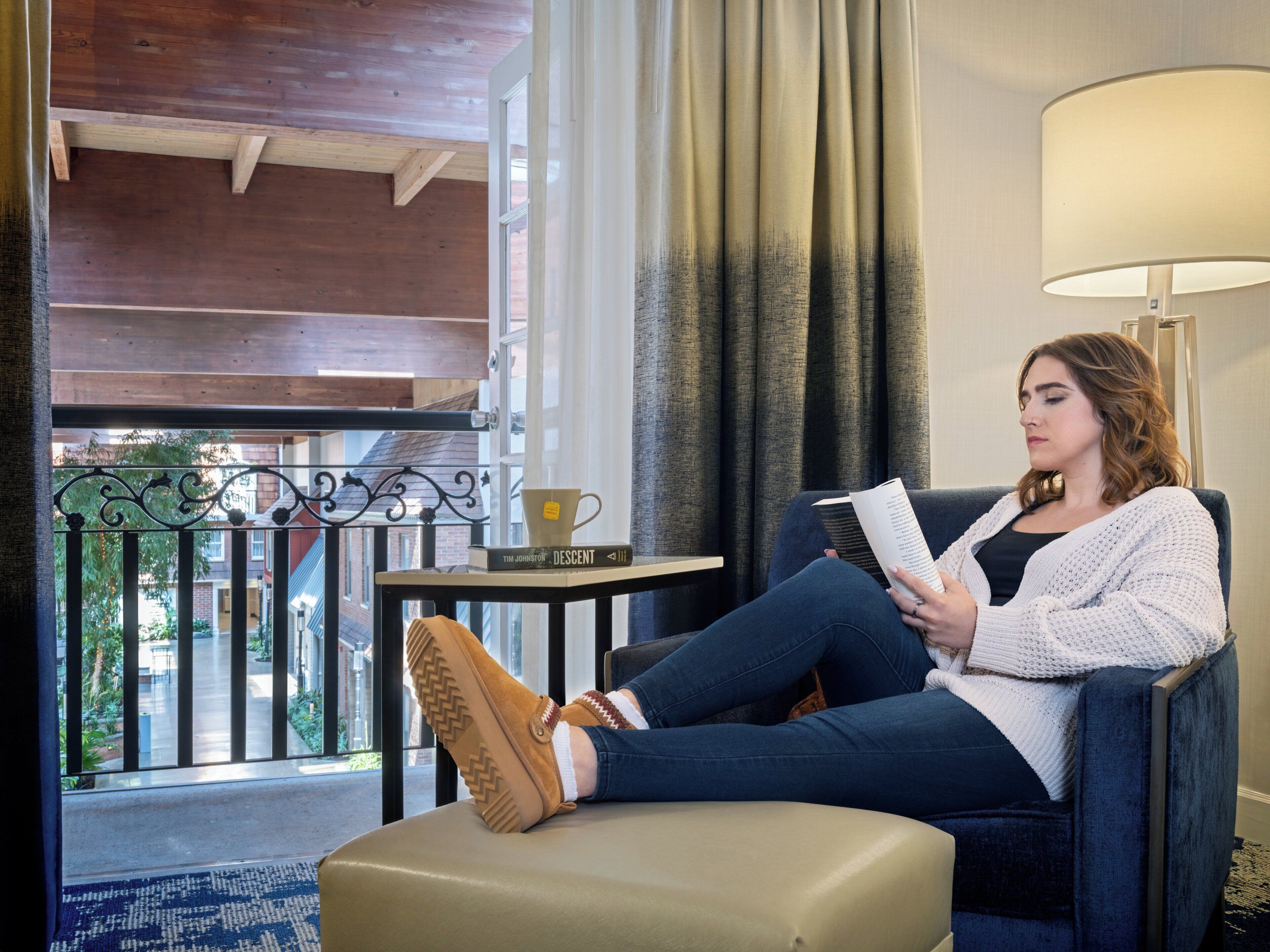 A person seated on a couch in a room with a view of a balcony and a window.