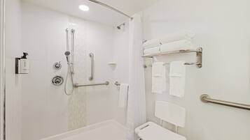 A shower with a handheld showerhead, a handheld shower control, a grab bar, and a white towel rack with towels.