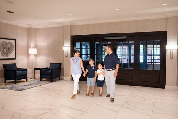 A family walking through a lobby with a large window, a framed artwork on the wall, and a floor lamp. - Crowne Plaza Albany - The Desmond Hotel by IHG (Albany)