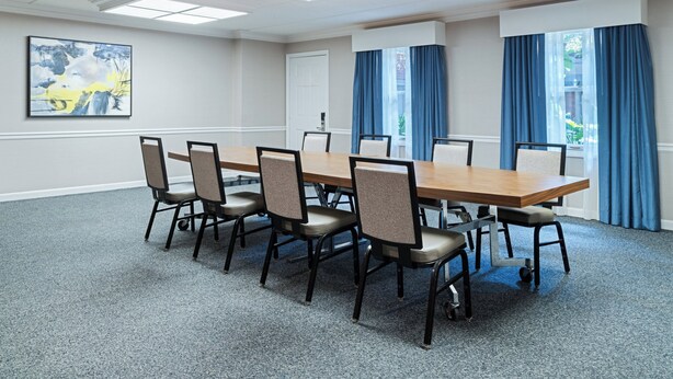 Une salle de conférence avec une longue table, six chaises et un tableau accroché au mur.