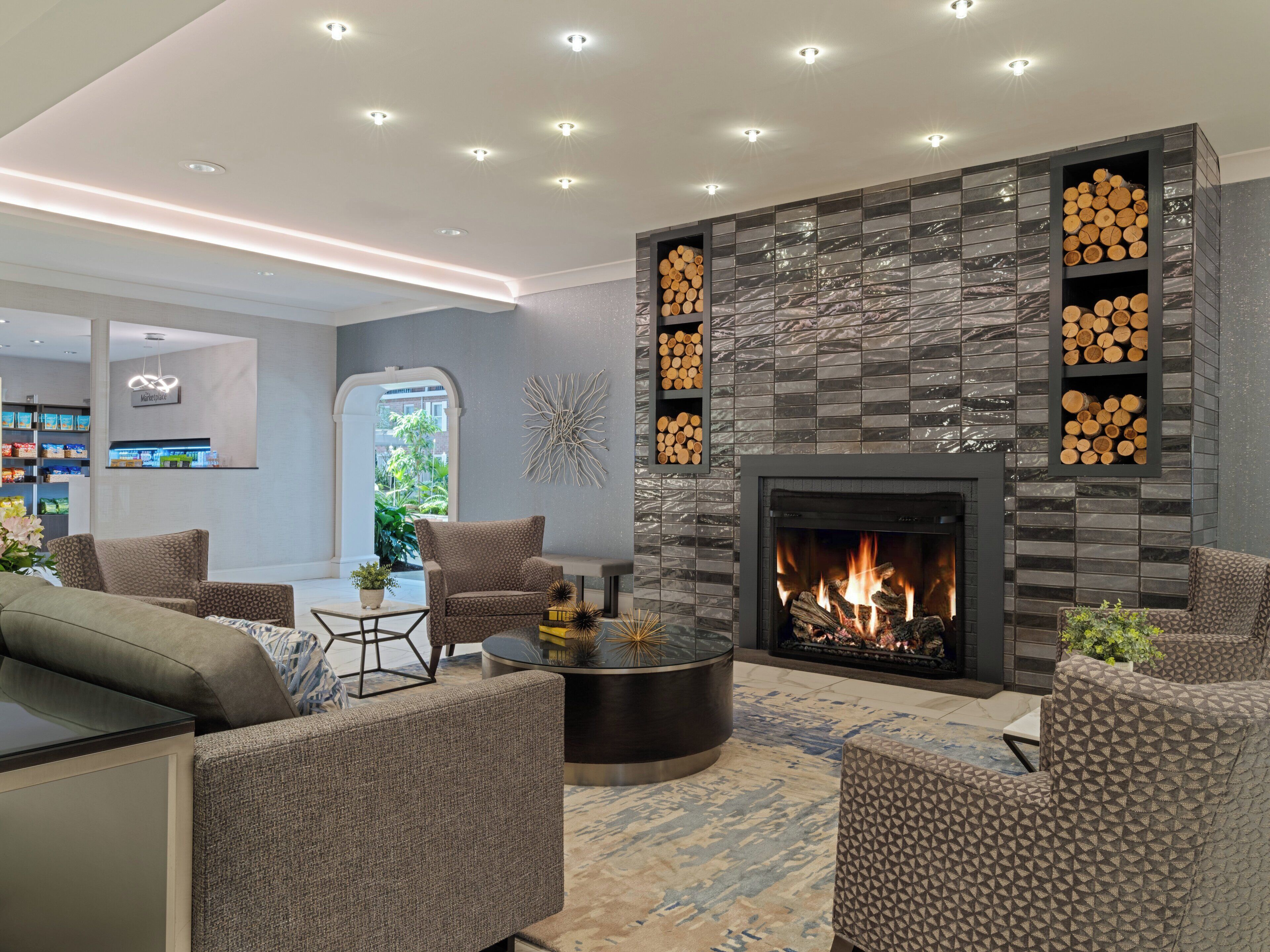 A modern living room with a fireplace, comfortable seating, and a view of the outdoors.
