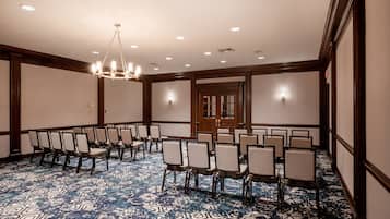 A conference room with rows of chairs, a patterned carpet, and a chandelier.