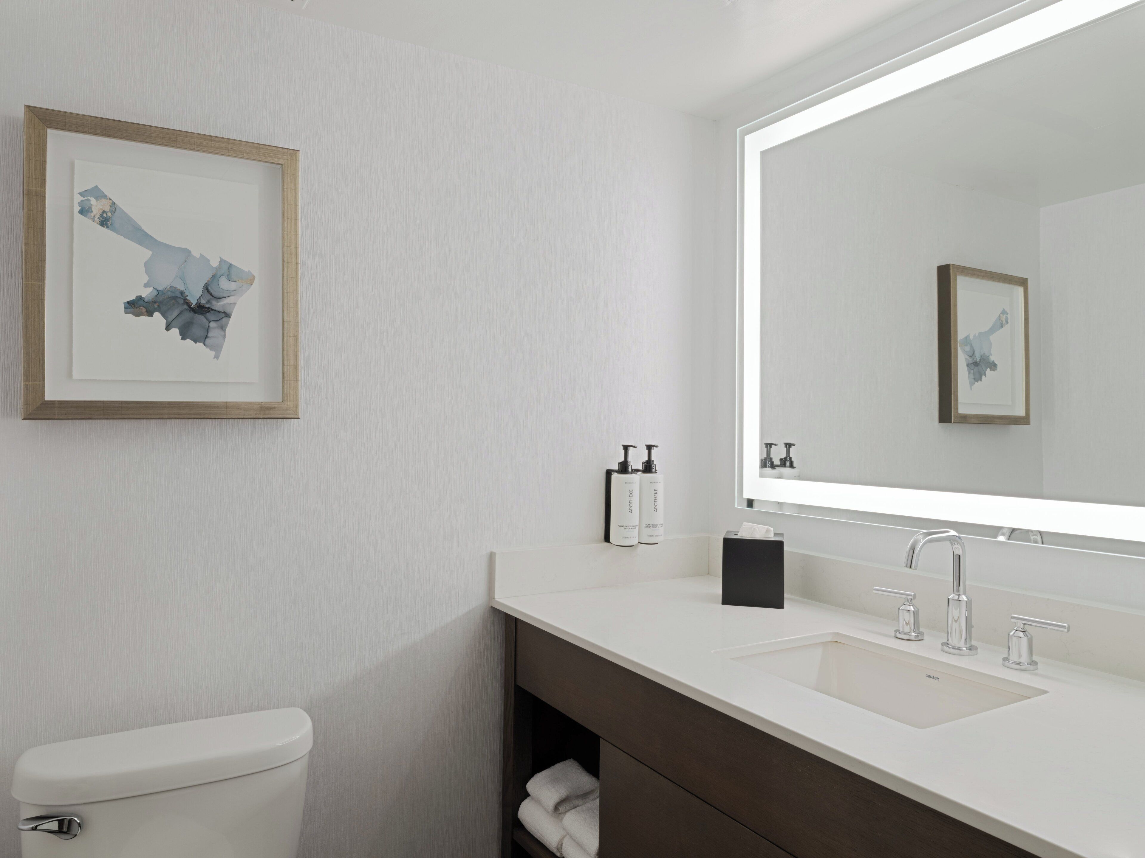 A modern bathroom with a white toilet, a large mirror, and a white sink with a dark vanity.