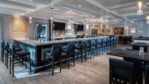 A modern bar area with a long counter, multiple bar stools, and a variety of bottles.