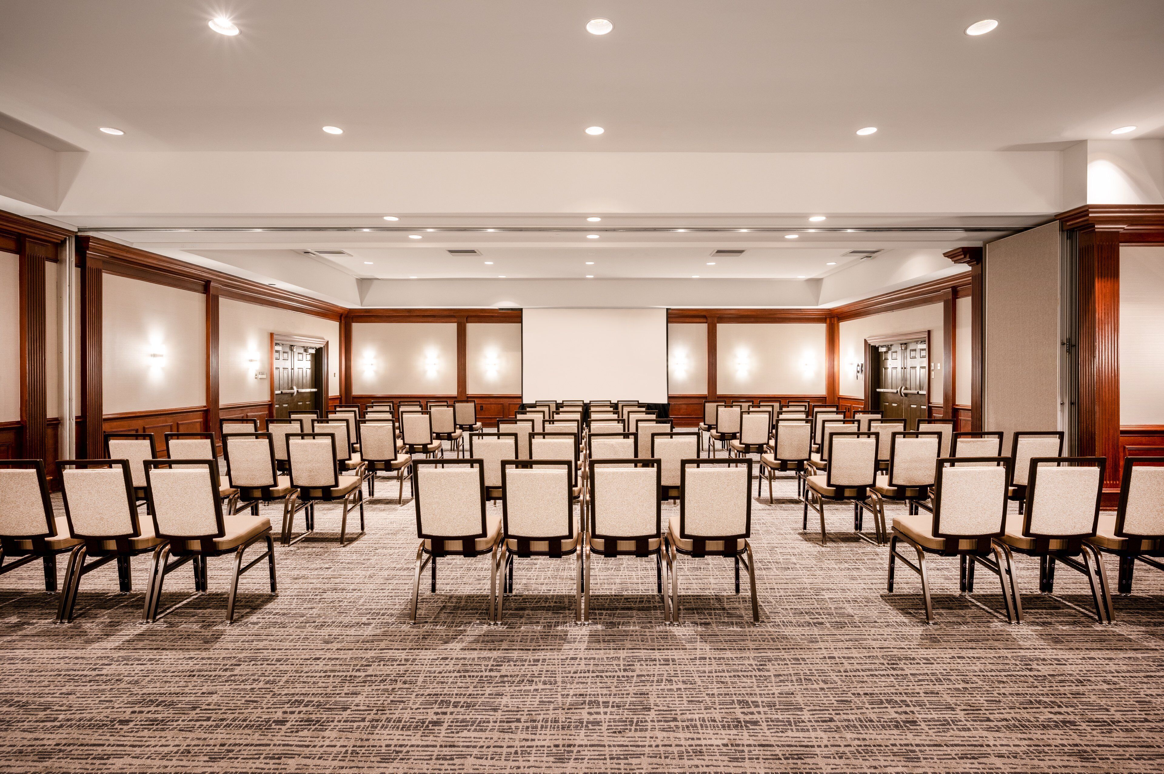 Un salón de conferencias con hileras de sillas, paneles de madera e iluminación empotrada.
