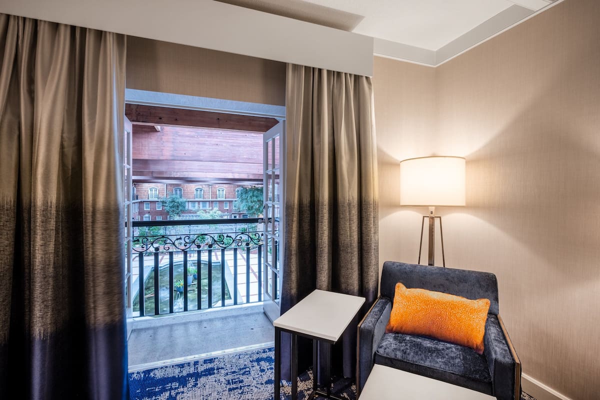 Een hotelkamer met een balkon, een bank, een klein tafeltje en een vloerlamp.