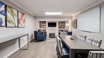 A modern conference room with a long table, blue and plaid chairs, a whiteboard, and abstract art on the walls.