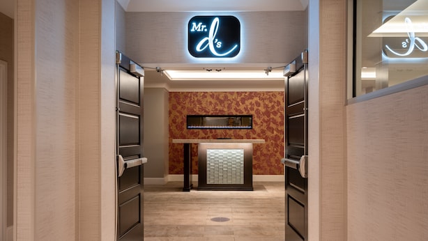 A modern hotel lobby with a reception desk, a neon sign above, and a patterned wall.