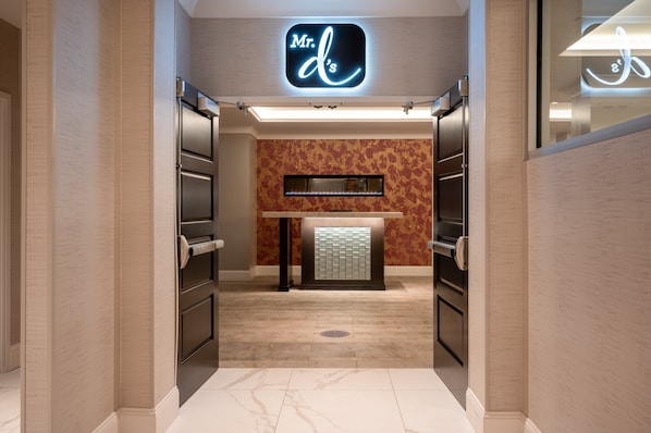A modern hotel lobby with a reception desk, a neon sign above, and a patterned wall.