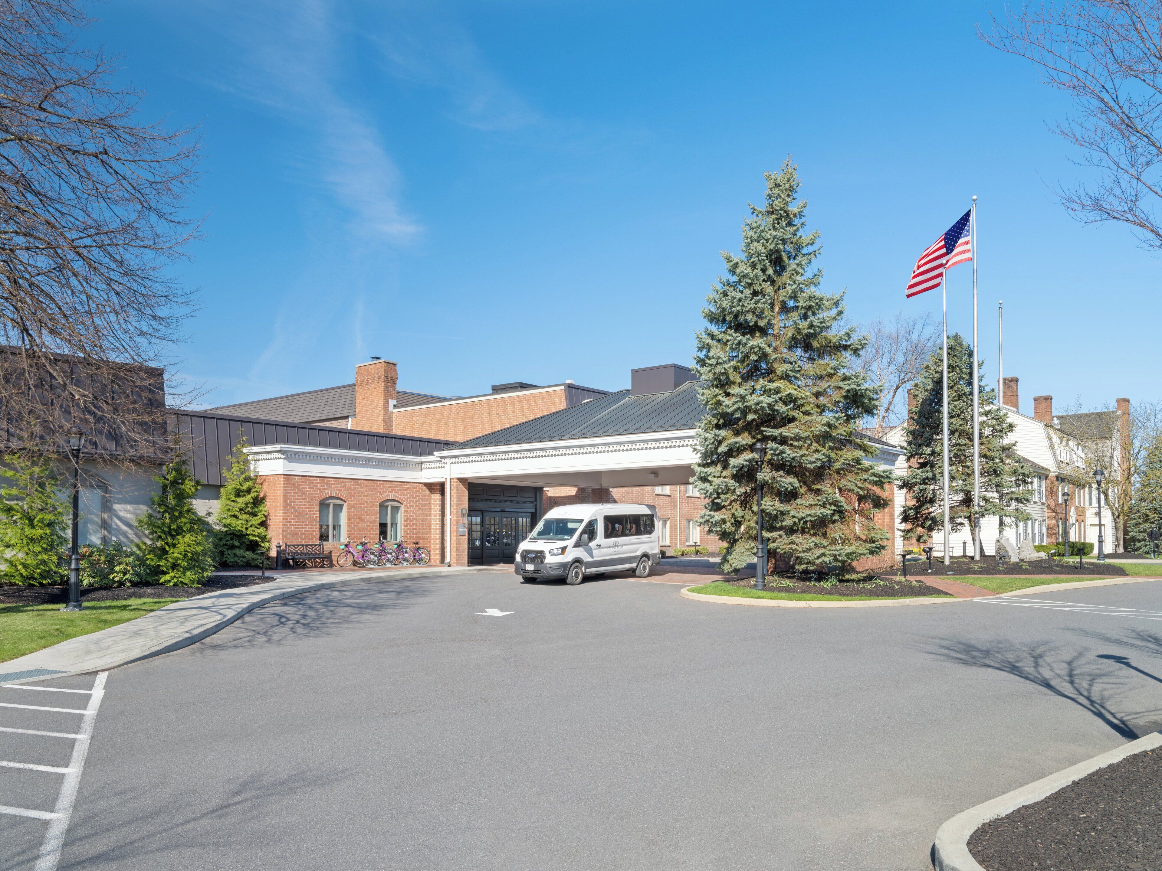 A building with a brick facade, a flagpole with an American flag, and a parked van.