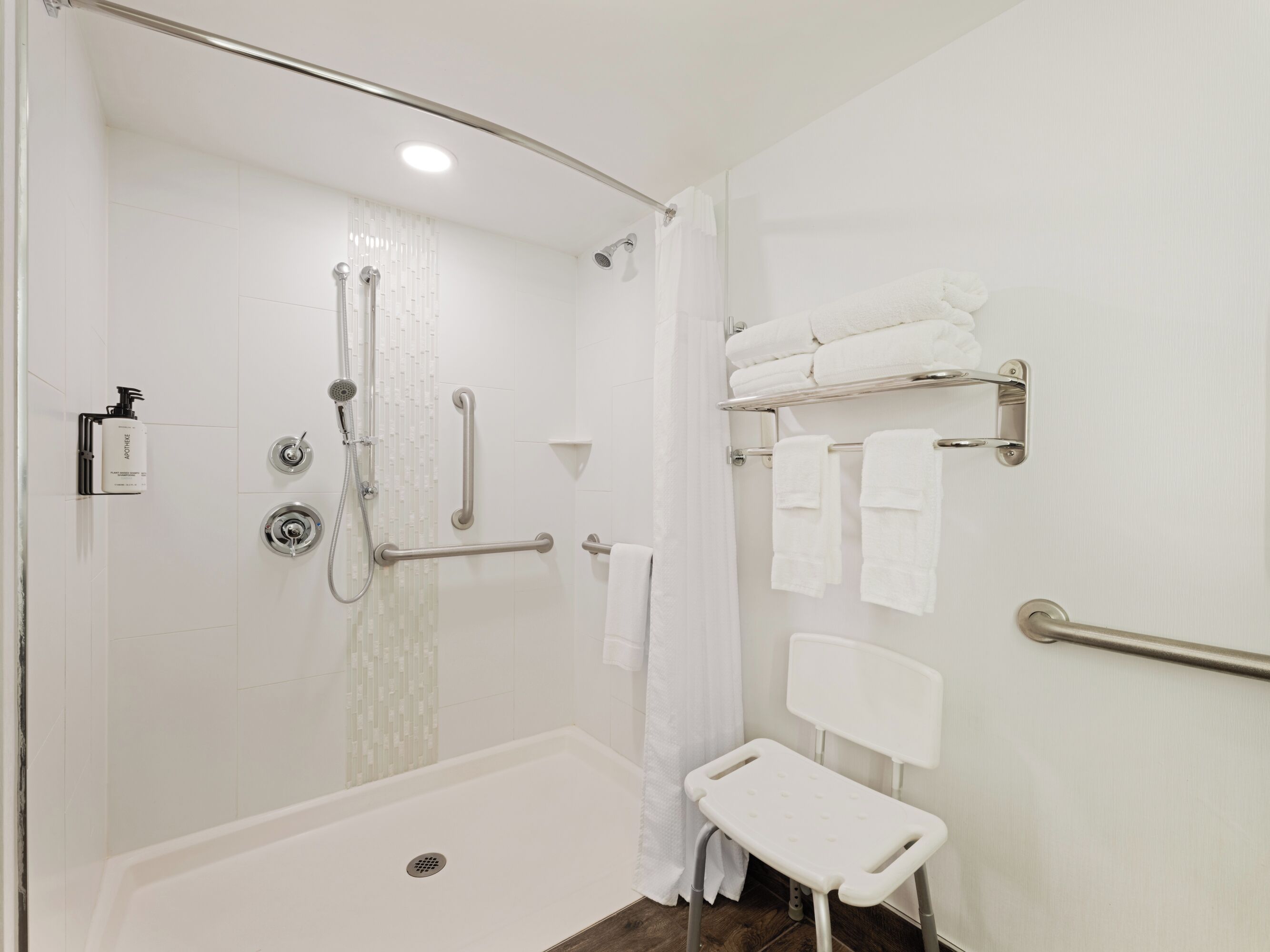 Un baño moderno con ducha a nivel, barras de apoyo, un banco blanco y un perchero para toallas.