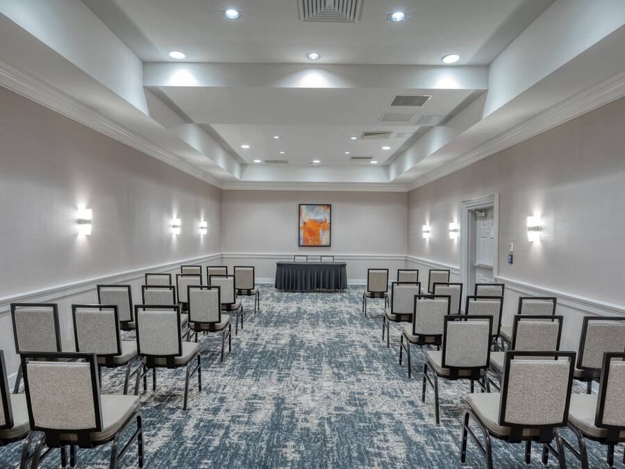 Uma sala de conferências com fileiras de cadeiras, um pódio e piso coberto de carpete.