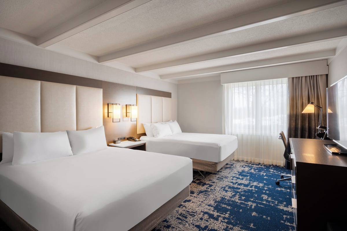 Een hotelkamer met twee bedden, een bureau en een groot raam met gordijnen.
