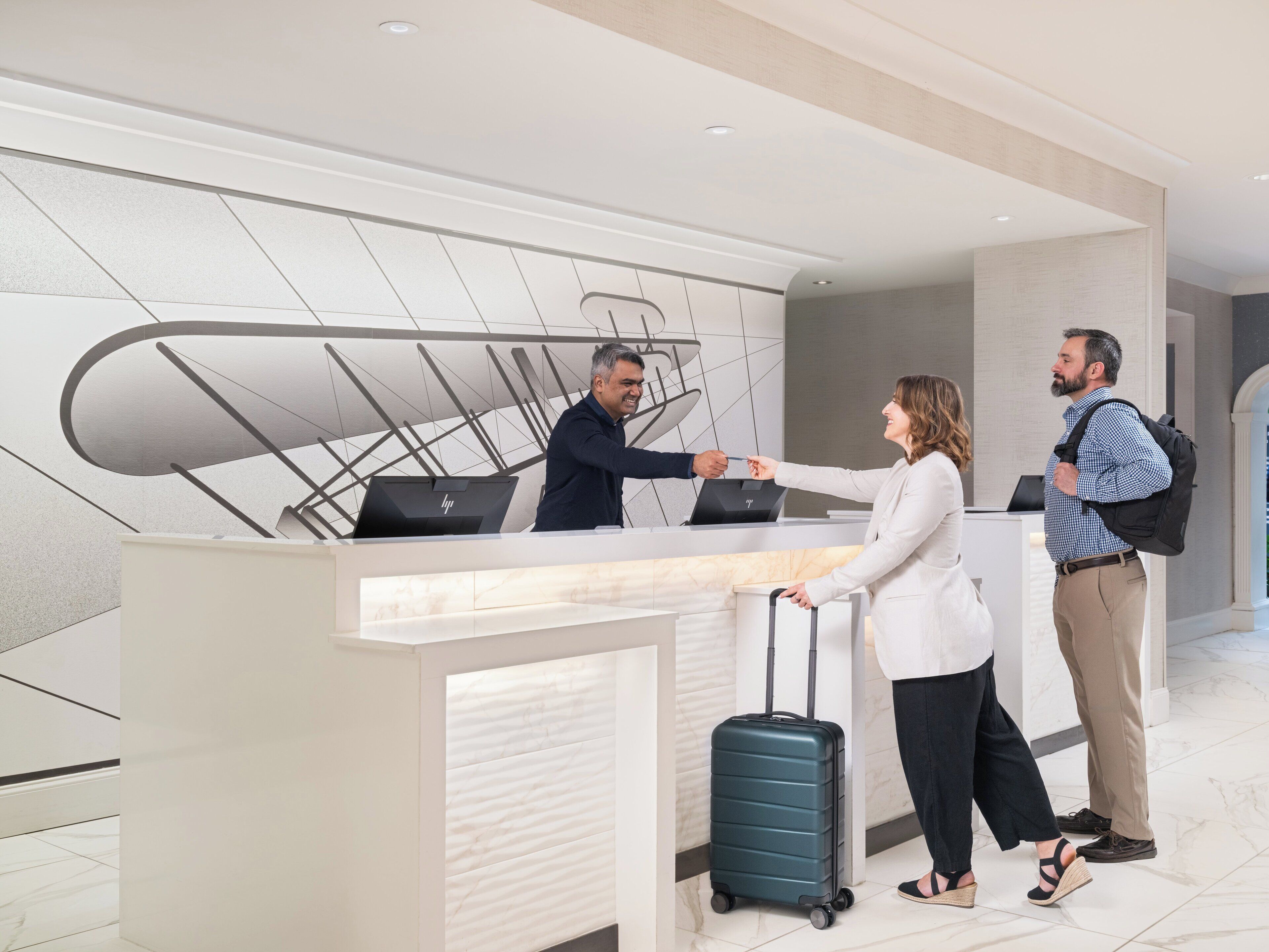 A reception desk with a modern design, a laptop on it, and a person with a suitcase.