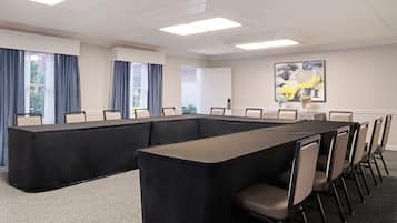 Un salón de conferencias con una larga mesa, sillas y un cuadro en la pared.