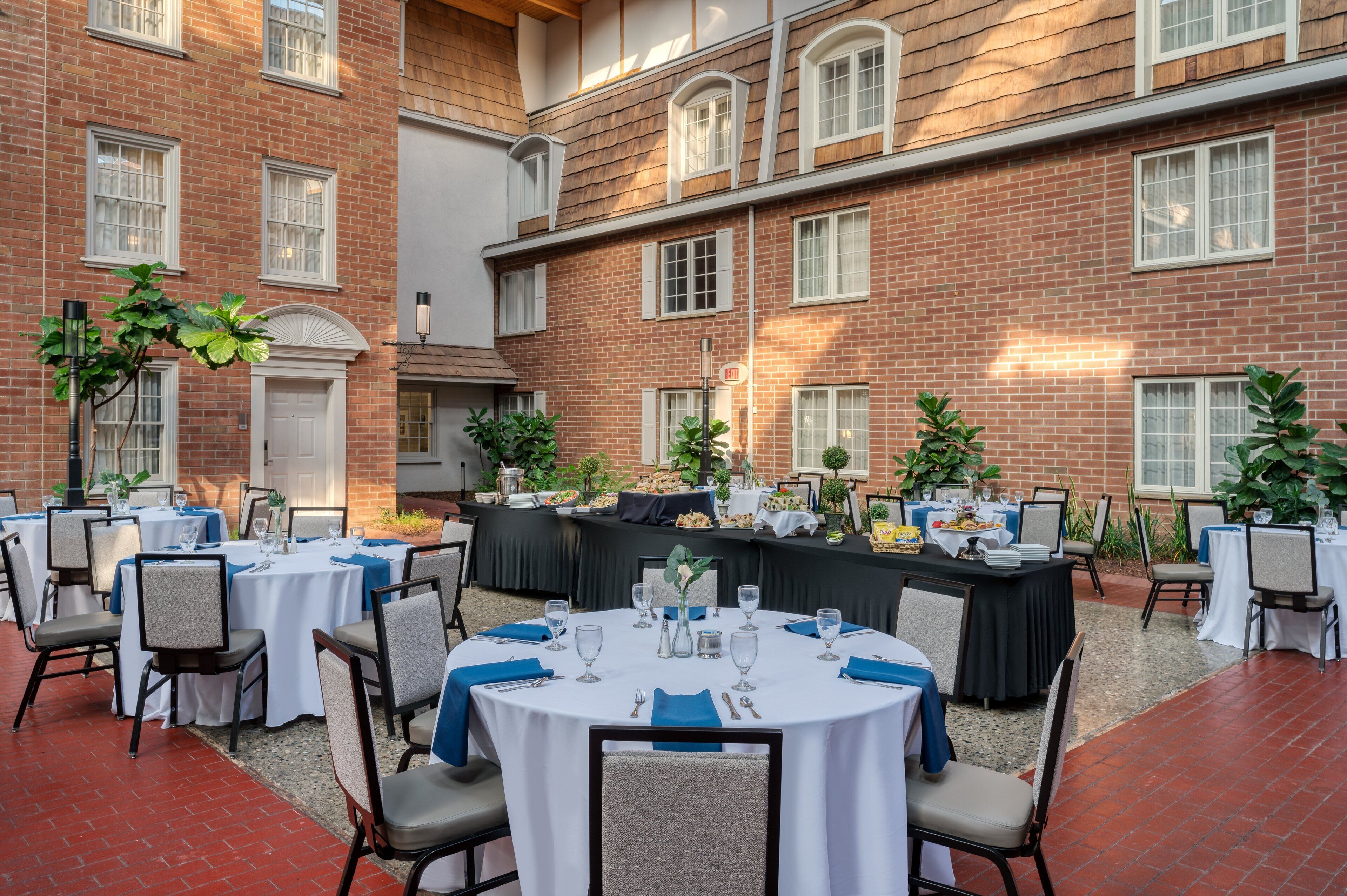 Une salle de banquet avec des tables rondes dressées pour un événement formel, entourée de murs en briques et de grandes fenêtres.