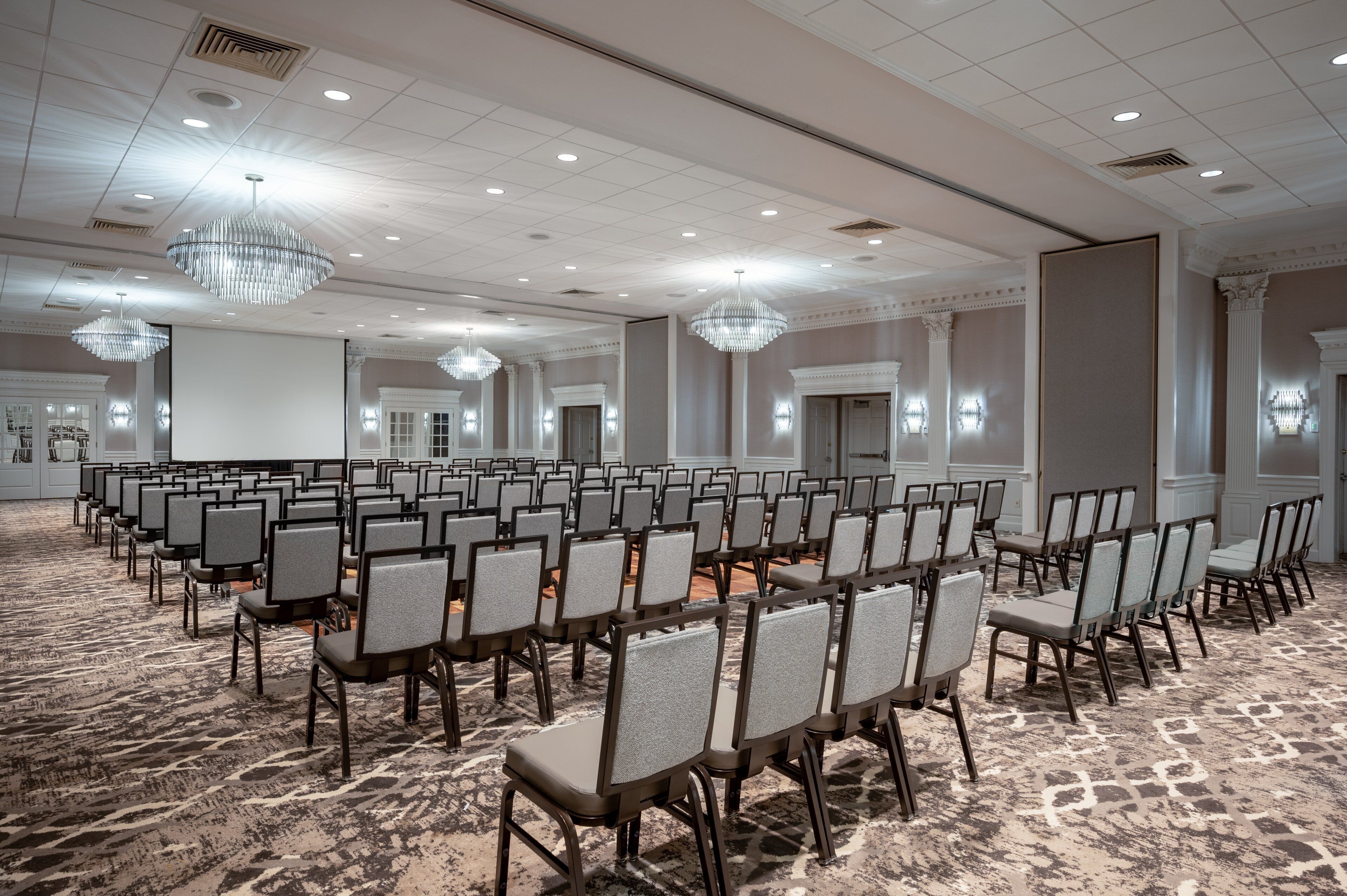 Un salón de conferencias con filas de sillas, candelabros y una alfombra estampada.