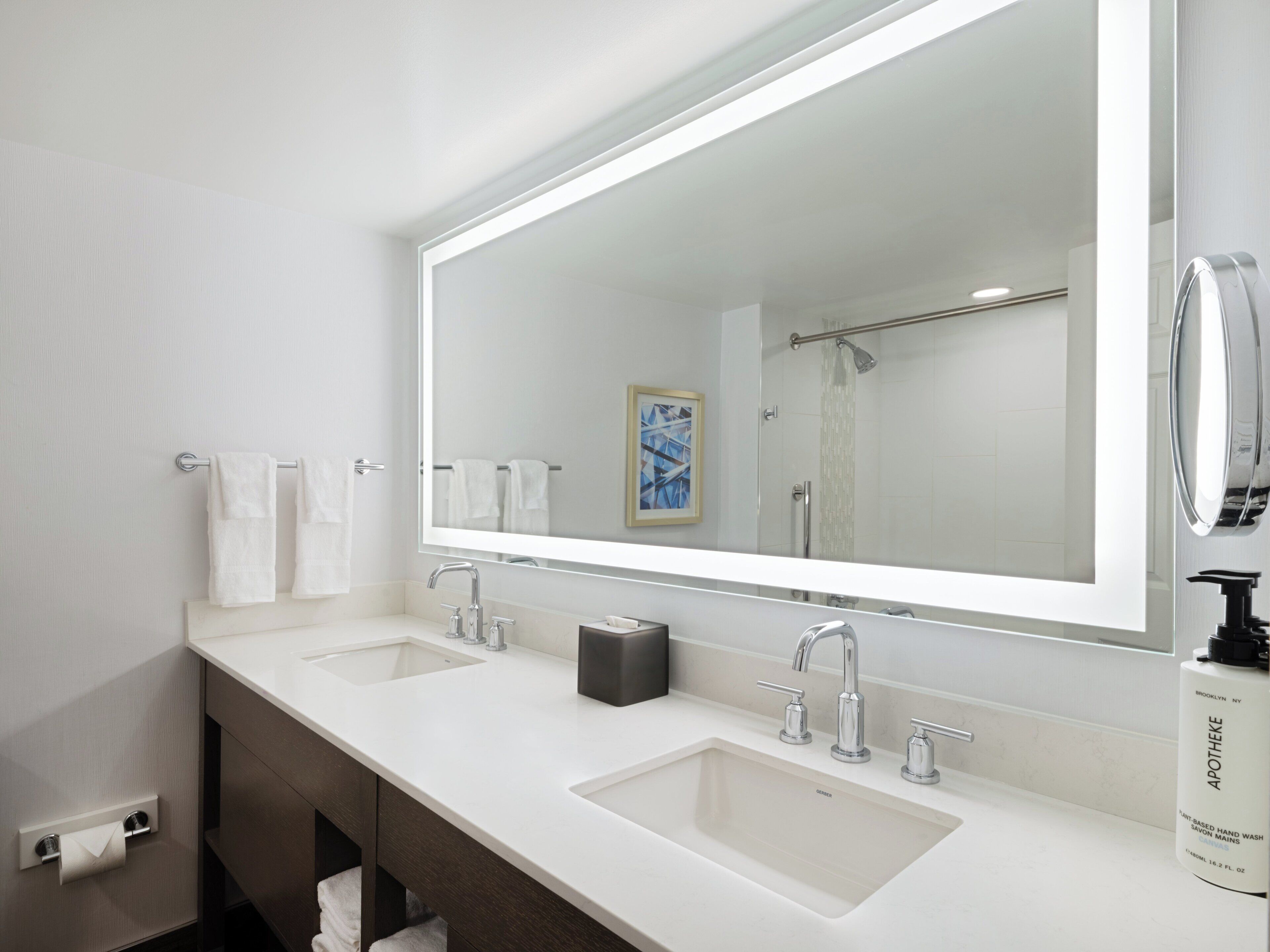 A modern bathroom with two sinks, a large mirror, and a towel rack.