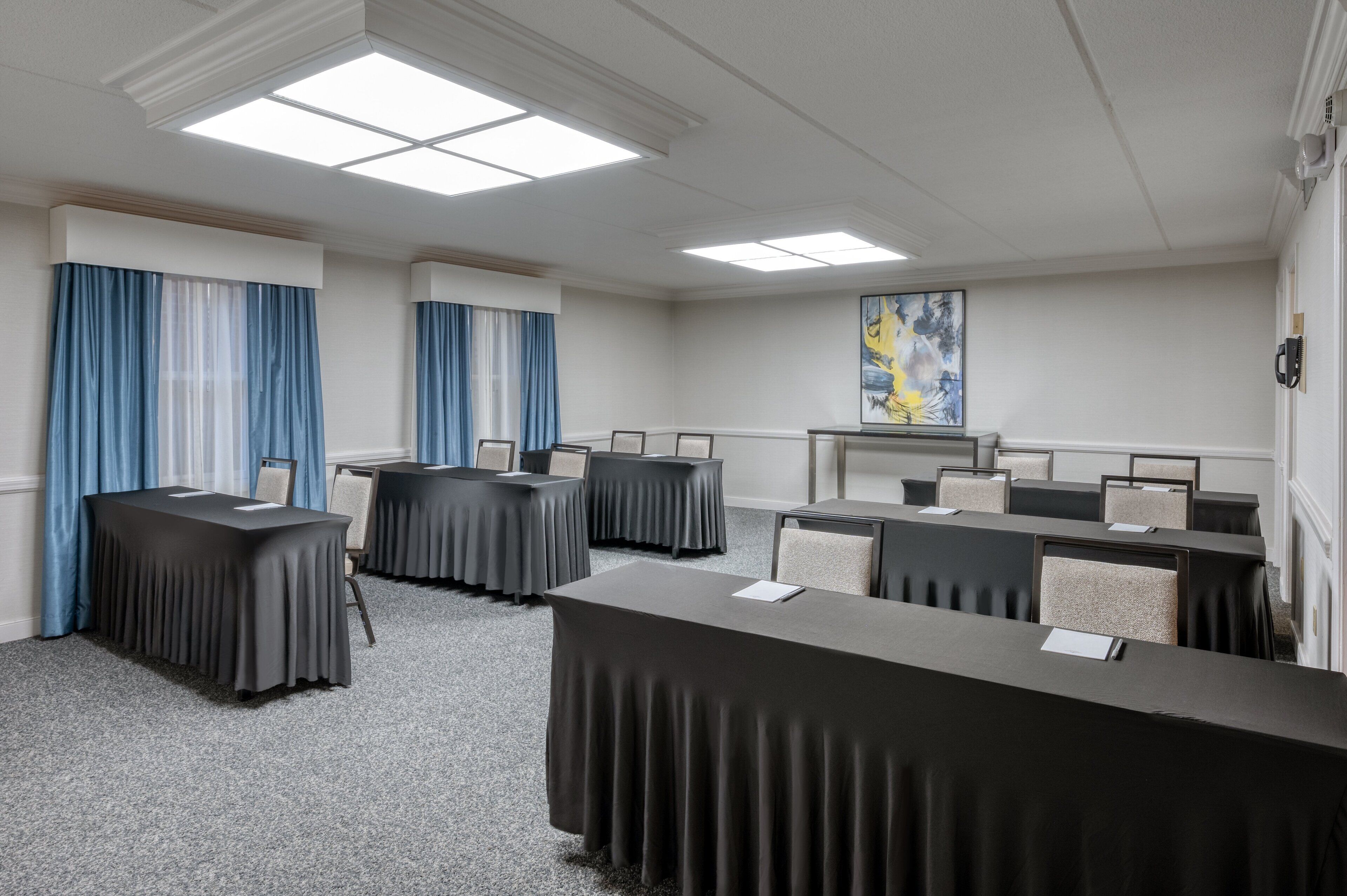 A conference room with tables and chairs, a painting on the wall, and a ceiling with recessed lighting.