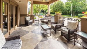 A covered patio with wicker furniture, a glass table, and a view of a green garden. - The Boulevard Inn & Bistro (Saint Joseph)