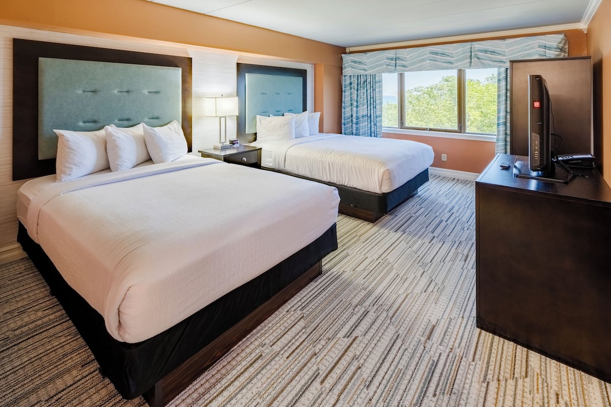 A hotel room with two beds, a desk with a computer, and a large window with curtains.