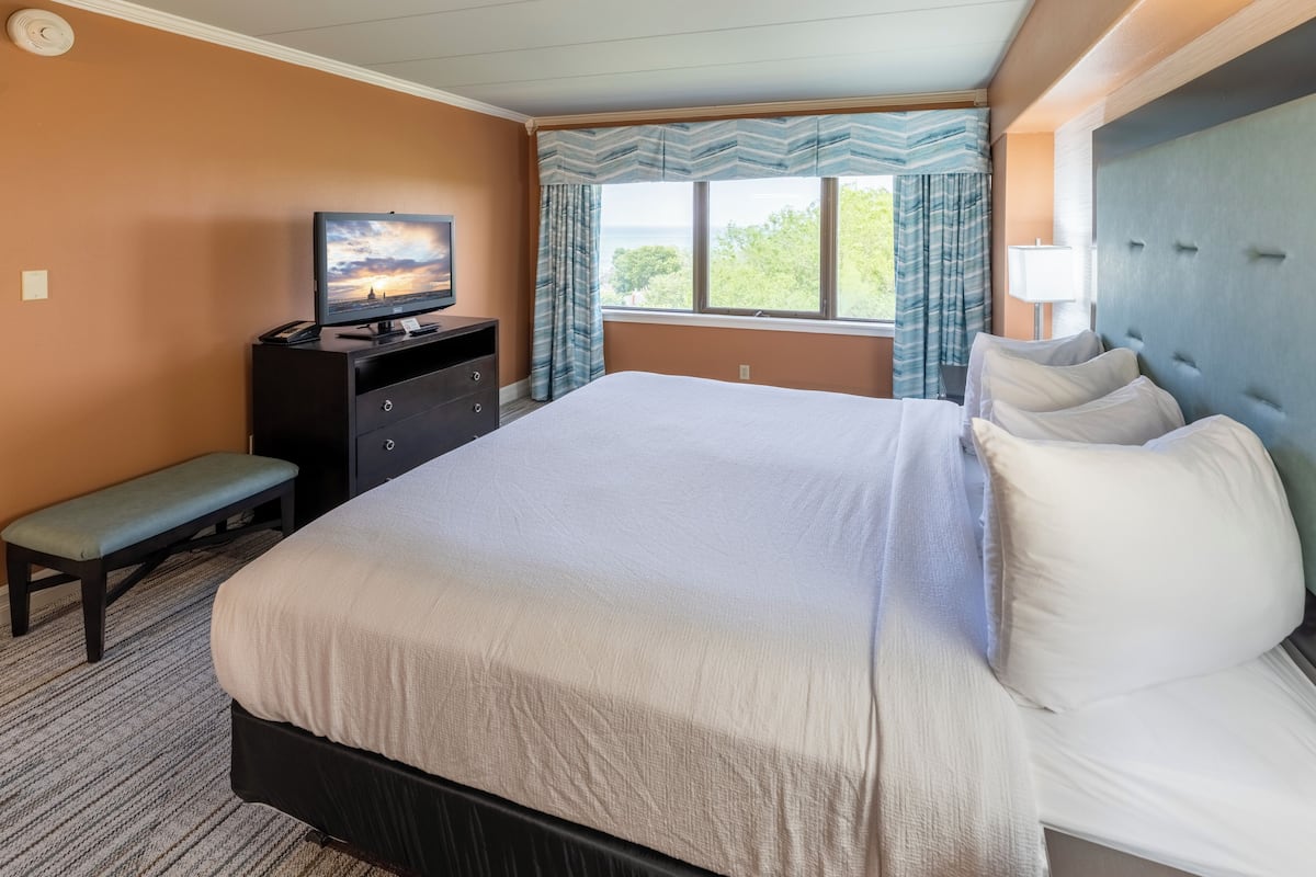 A hotel room with a large bed, a desk with a television, a bench, and a window with curtains.