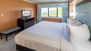 A hotel room with a large bed, a desk with a television, a bench, and a window with curtains.
