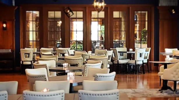 A spacious dining area with multiple tables and chairs, large windows, and decorative lighting fixtures. - The Boulevard Inn & Bistro (Saint Joseph)