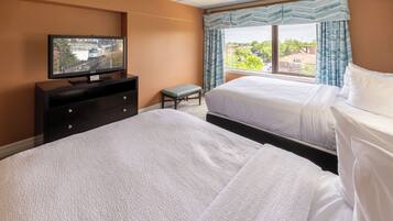 A hotel room with two beds, a television on a dresser, a bench, and a window with curtains.