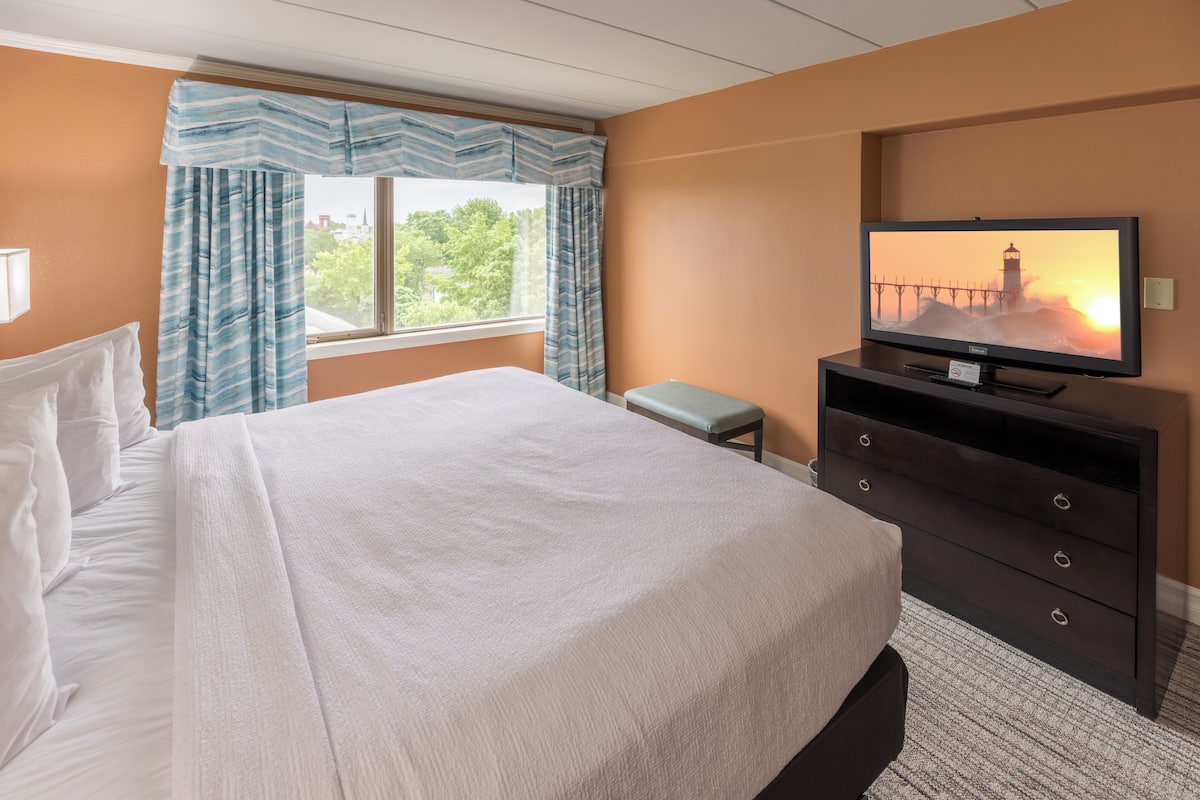 A hotel room with a large bed, a television on a dresser, and a window with curtains.