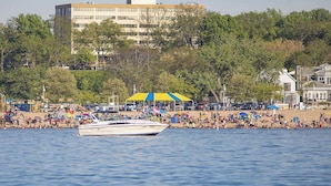 A waterfront hotel with a large building in the background, a beach with people and umbrellas, and a boat in the water. - The Boulevard Inn & Bistro (Saint Joseph)