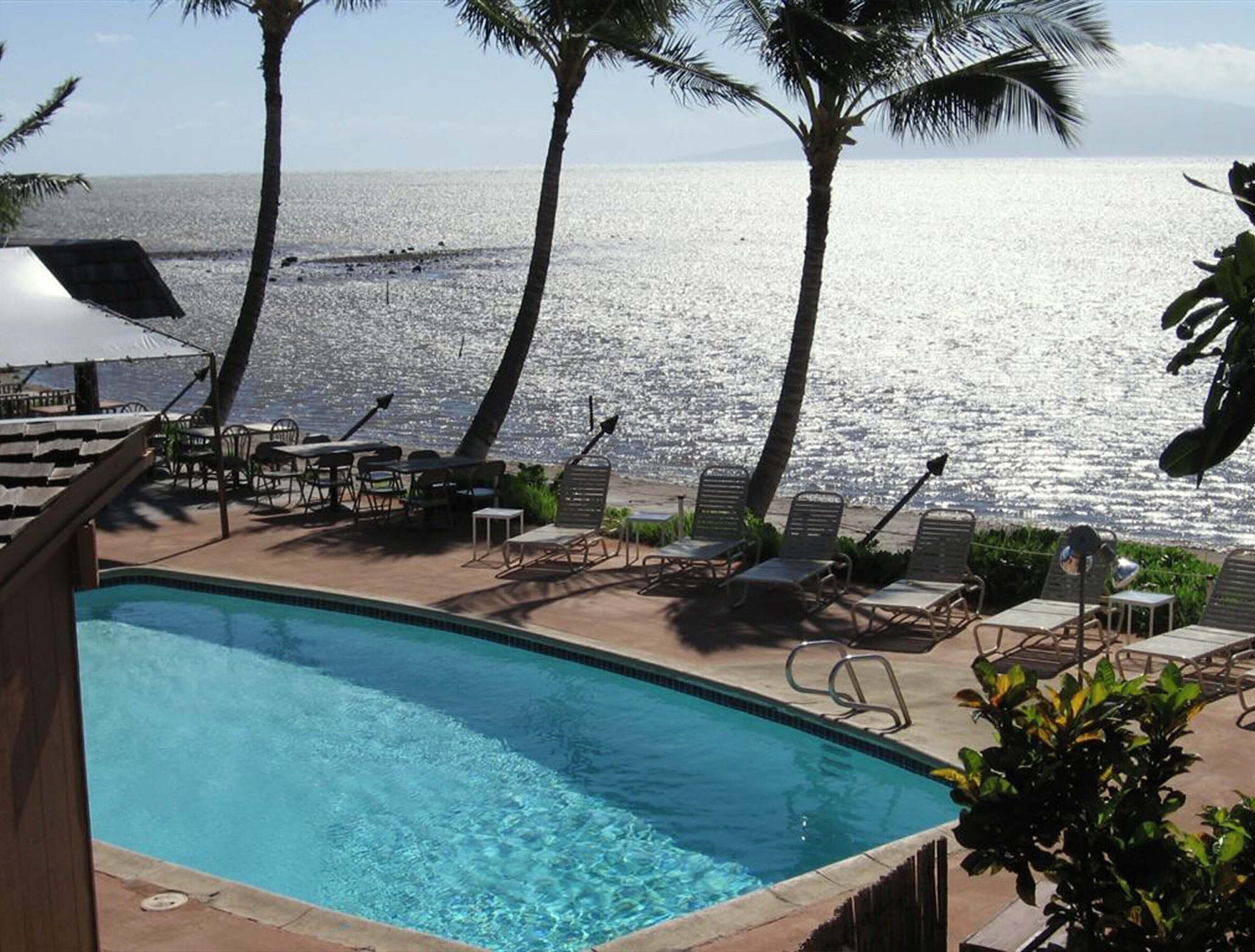 A pool area with lounge chairs and tables, overlooking a beach and the ocean.